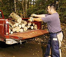 A man dressed in safety vest loads logs into the back of a pickup truck